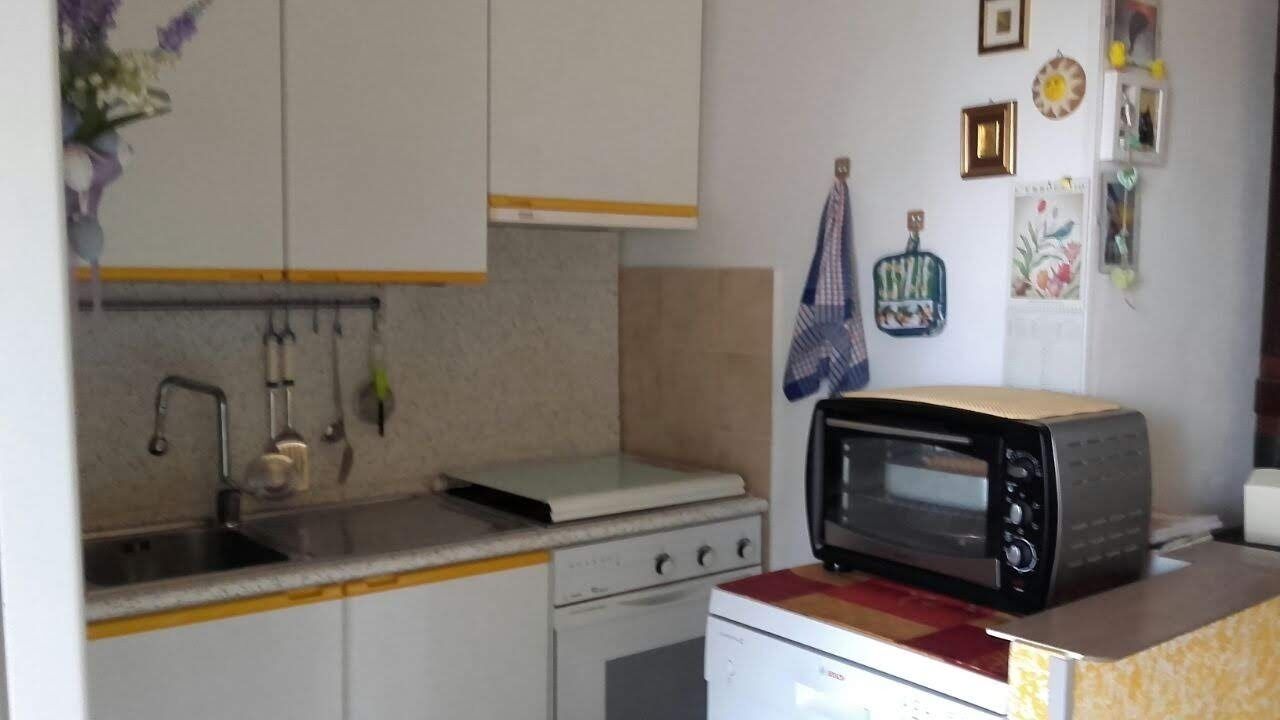 Una cocina compacta con armarios blancos, microondas, estufa y pileta.