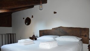 Un lit bien fait, avec du linge de lit blanc et des serviettes pliées, une tête de lit en bois, une table de chevet avec une lampe et un miroir fixé au mur.