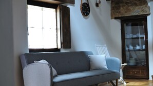 Un salon moderne avec un canapé gris, un fauteuil blanc, un meuble en bois doté de portes en verre et un mur en pierre.