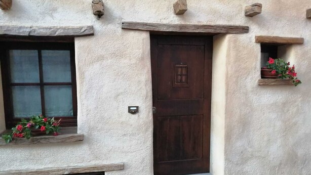 Un bâtiment rustique avec une porte en bois, une fenêtre agrémentée d’une jardinière et une petite fenêtre ornée d’une grille métallique.