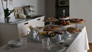 Une table à manger dressée avec différents plats et un service à thé, entourée d’appareils de cuisine et d’une plante en pot.