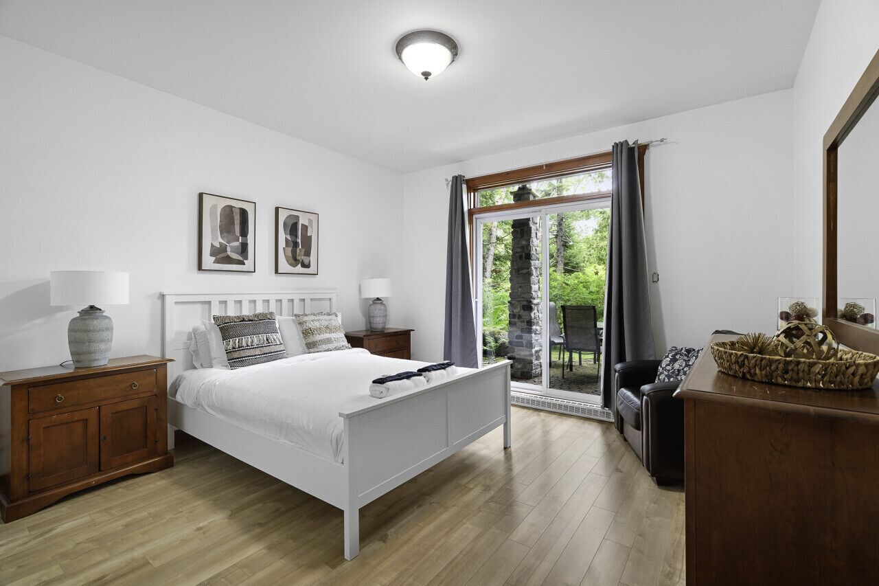 Quarto com cama, mesas de cabeceira, penteadeira e janela com cortinas.