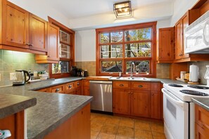 A kitchen with wooden cabinets, a dishwasher, a stove, and a window with a view of trees.