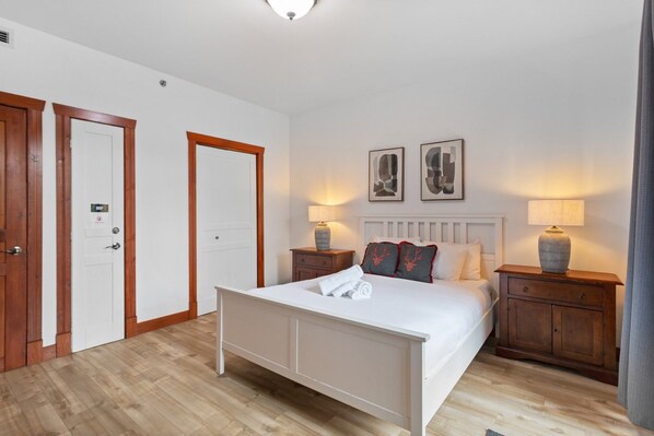 A hotel room with a bed, two bedside tables, a nightstand, a door, and a light fixture.