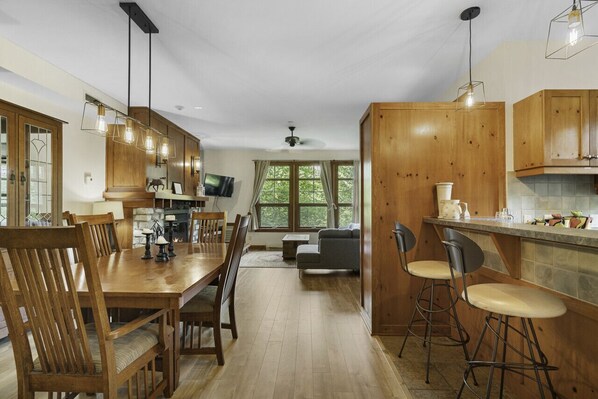 Una cocina moderna con armarios de madera, un comedor con mesa y sillas de madera, y una barra con taburetes.