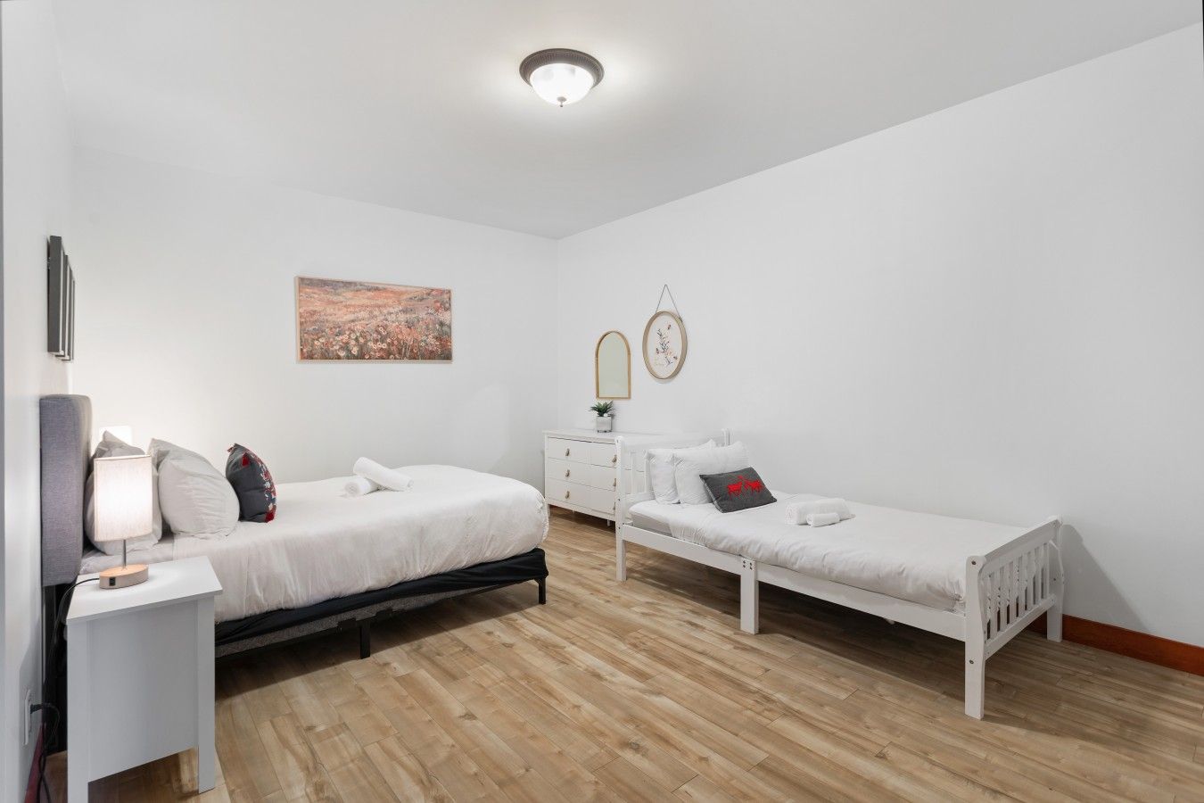 A bedroom with two single beds, a bedside table with a lamp, a dresser, and a painting on the wall.