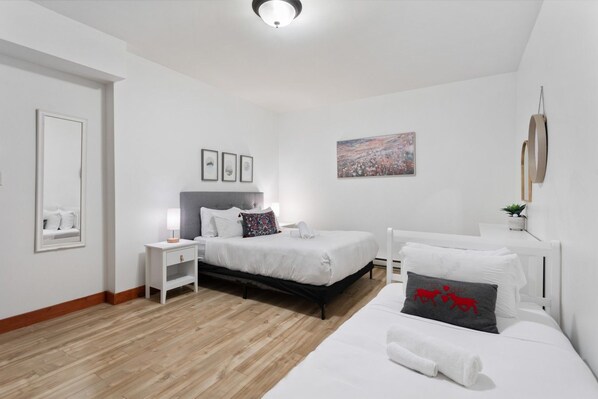 Un dormitorio moderno con una cama grande, una cama individual, una mesita de noche, un tocador, un espejo y un cuadro en la pared.