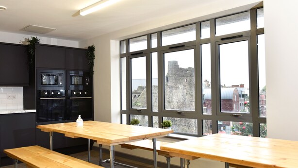 Une cuisine moderne dotée d’appareils électroménagers intégrés, de grandes fenêtres offrant une vue sur un bâtiment historique, et d’une table en bois avec des bancs.