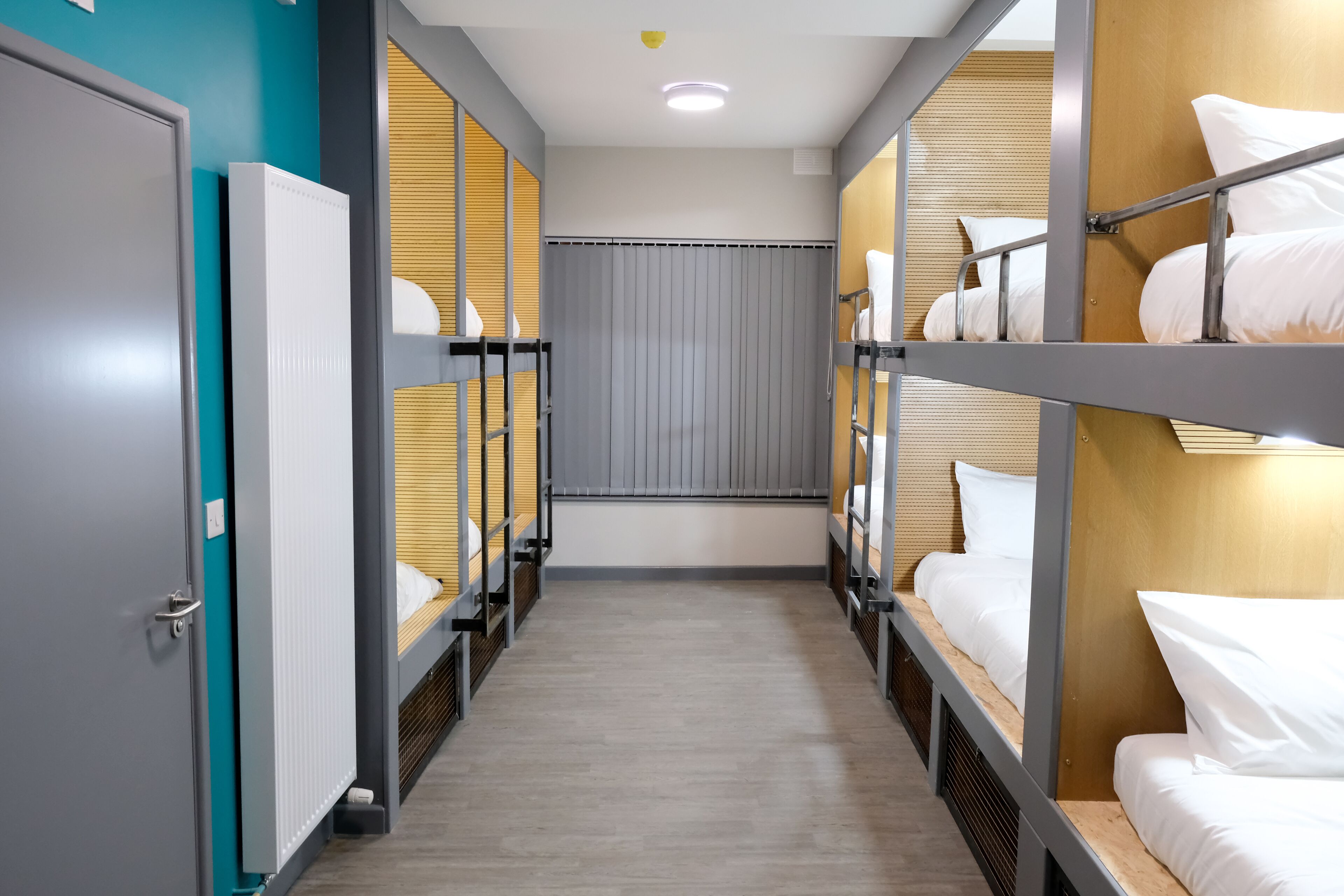 A corridor with bunk beds, wooden panels, and a grey door.
