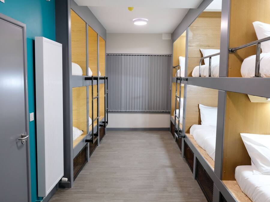 A corridor with bunk beds, wooden panels, and a grey door.