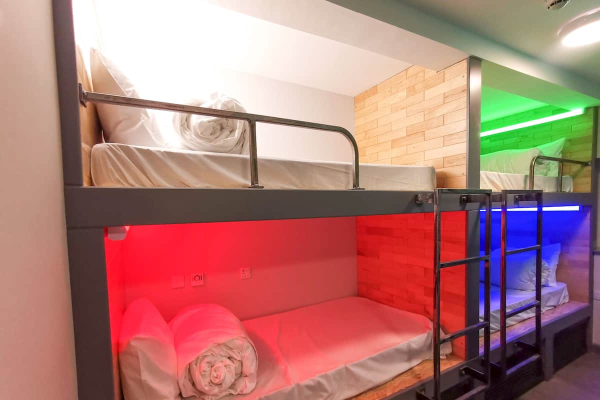 A bunk bed room with a wooden headboard, a red-lit lower bunk, and a green-lit upper bunk.