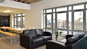 Un espace de bureau moderne avec un canapé en cuir noir, des tables en bois et de grandes fenêtres donnant sur la ville.
