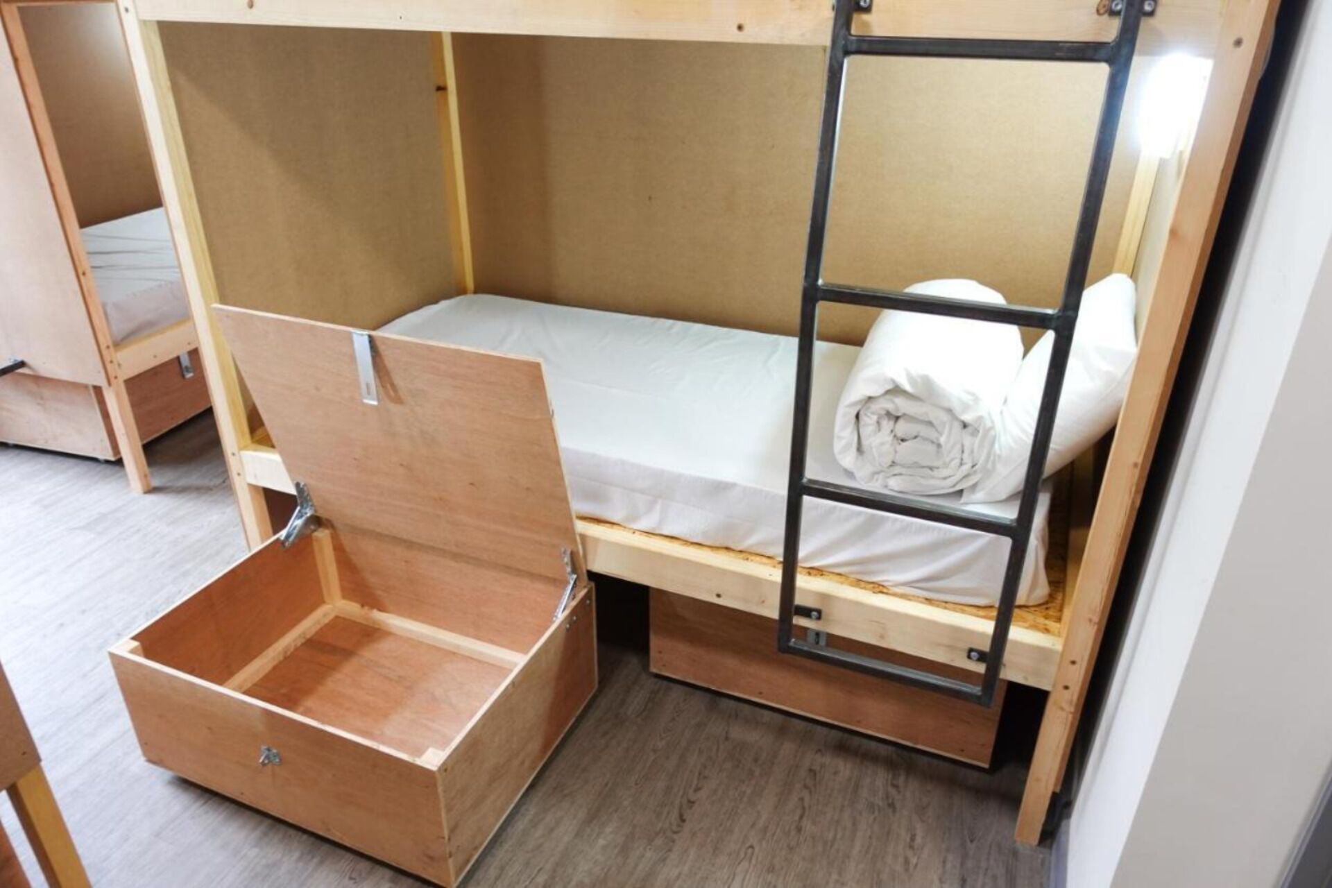 Ein platzsparendes Etagenbett mit ausziehbarer Schublade darunter, einer kleinen Ablagefläche und einem weißen Lattenrost.