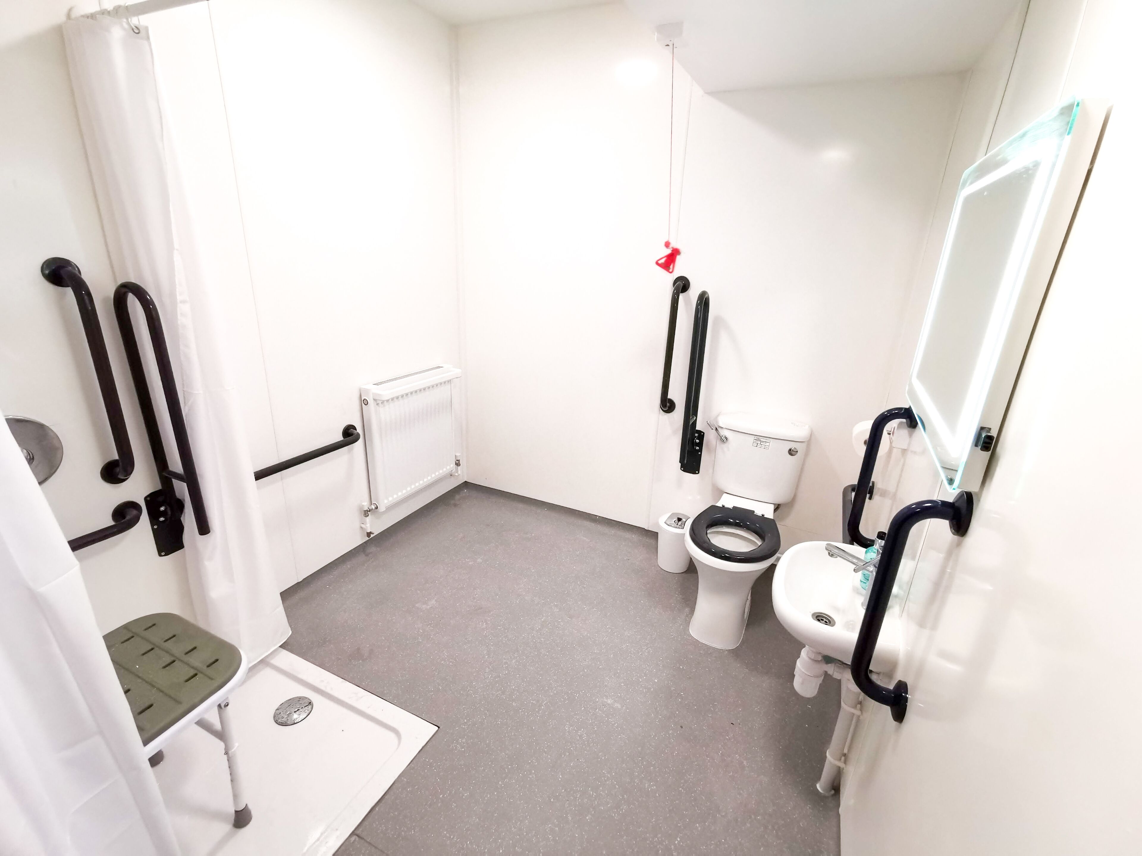 A small, white bathroom with a toilet, bidet, and sink. It includes a step stool and handrails for accessibility.