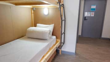 A bunk bed with a ladder, a wooden headboard, and a white mattress. There is a door with a sign on it and a wooden floor.