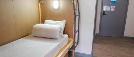 A bunk bed with a ladder, a wooden headboard, and a white mattress. There is a door with a sign on it and a wooden floor.