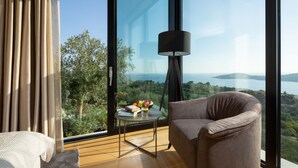 Een moderne kamer met een groot raam, een bruine fauteuil, een klein tafeltje met een lamp en uitzicht op een landschap.