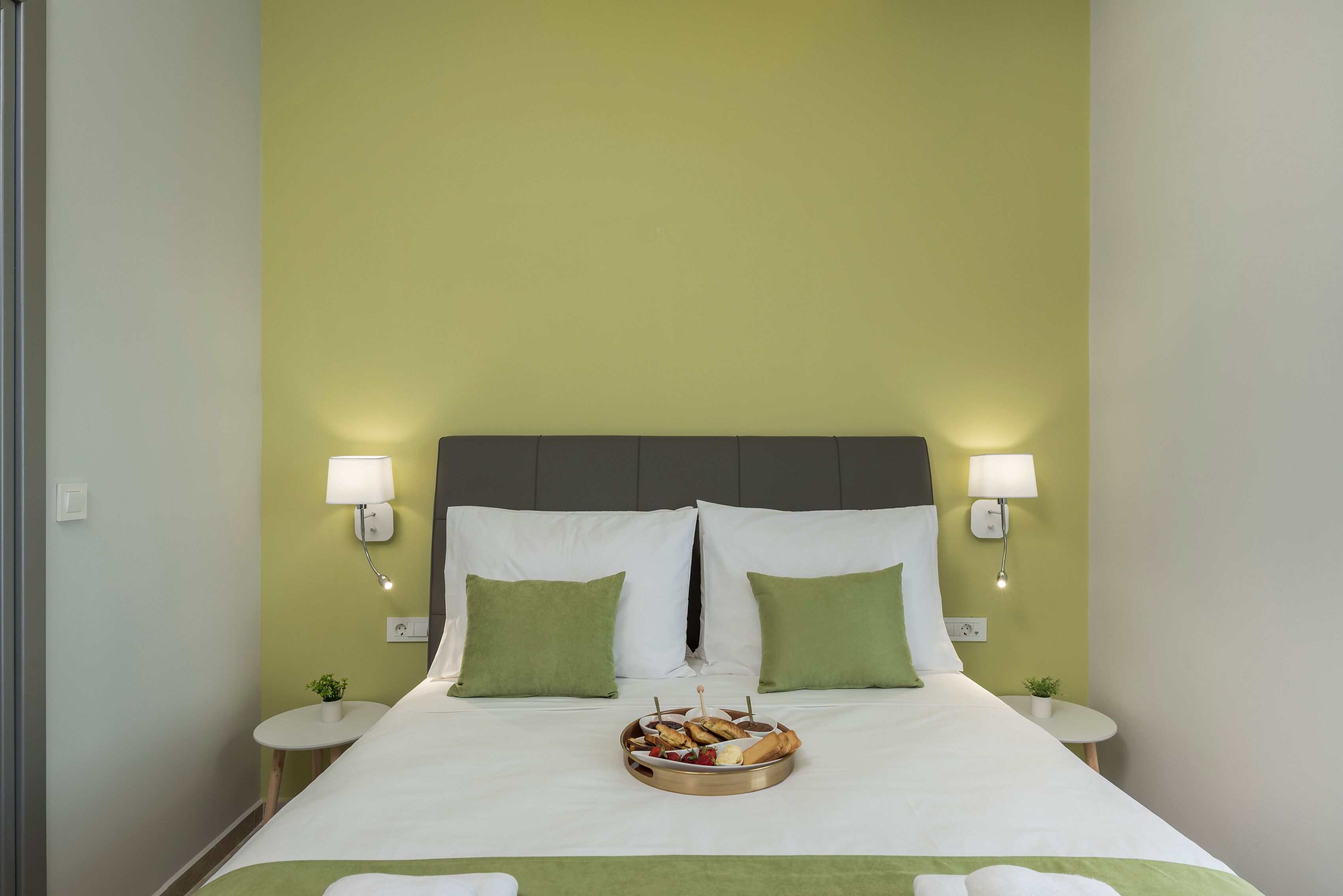 A neatly made bed with a tray of snacks, two green pillows, and bedside lamps.