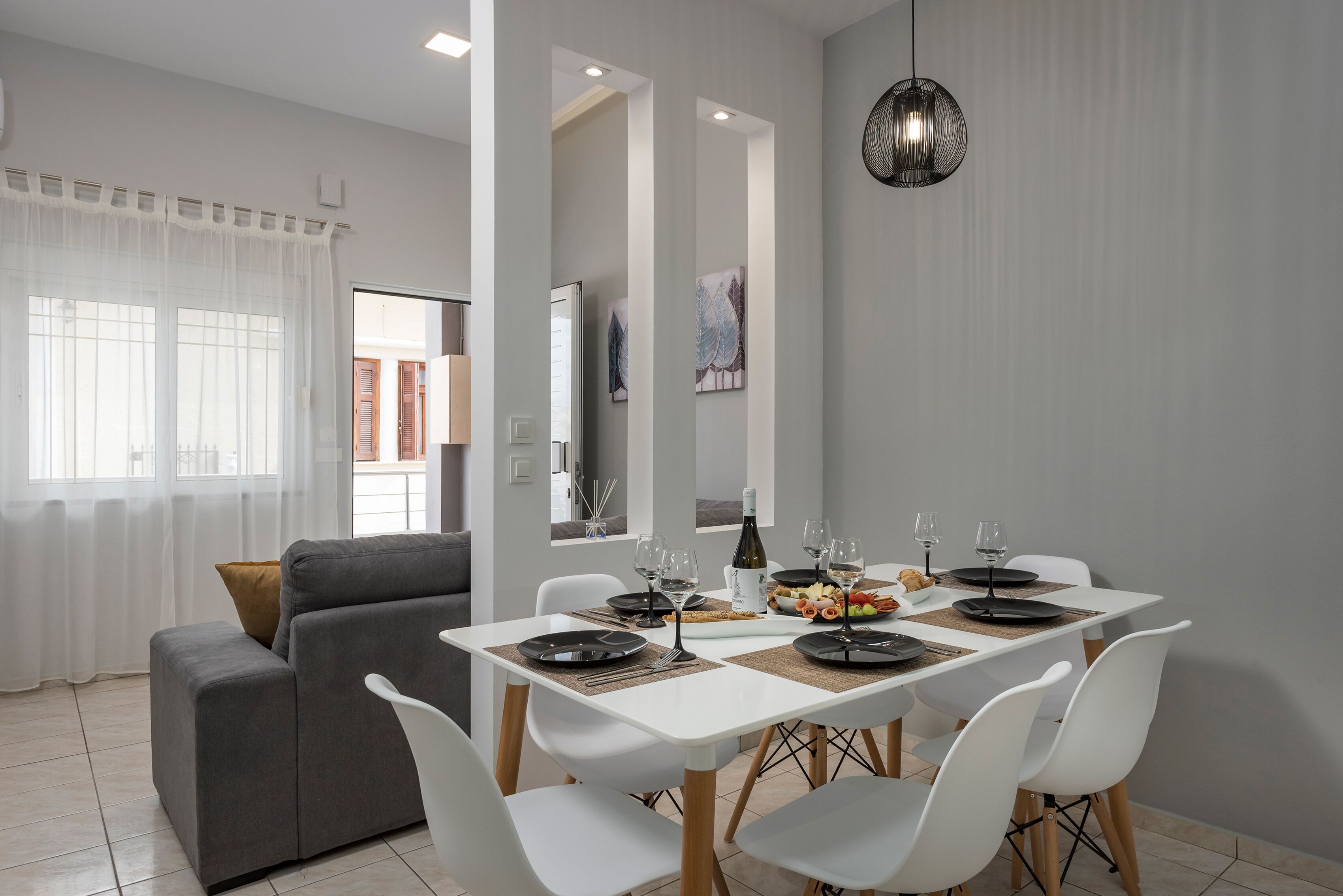 A modern dining area with a white table set for six, white chairs, and a grey sofa.