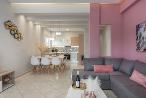 Una sala de estar moderna con un sofá gris, un comedor con sillas blancas y una cocina al fondo.