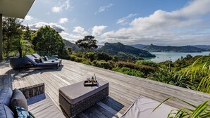 A wooden deck with a sofa and a table, overlooking a bay with boats and hills. - KAURI HILL ESTATE Luxe Retreat Overlooking Whangaroa Harbour (Northland)