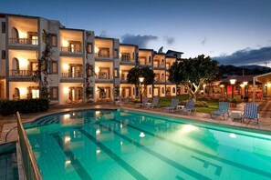 A hotel with a swimming pool, multiple balconies, and outdoor seating areas. - Fan Village (Hersonissos)