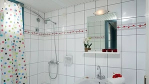 A bathroom with white tiled walls, a shower with a handheld showerhead, a sink with a mirror above it, and a towel rack. - Fan Village (Hersonissos)