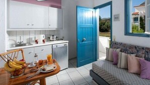 A compact kitchen with white cabinets, a blue door, and a dining area with breakfast items. - Fan Village (Hersonissos)