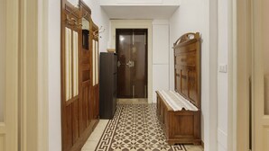 A narrow hallway with wooden doors, a bench, and patterned flooring. - Hostmate - Milano - Ozieri (Milano)