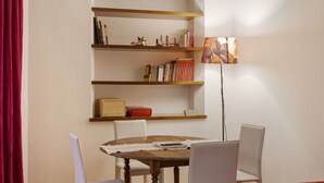 A room with a wooden table, white chairs, a bookshelf with books and decorative items, and a floor lamp. - Hostmate - Milano - Ozieri (Milano)