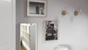 A room with a white door, a framed cityscape, a framed tram, and two wall-mounted light fixtures. - Hostmate - Milano - Farini - Garibaldi (Milano)