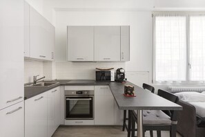 Una cocina compacta con armarios blancos, horno integrado y un comedor con mesa y sillas.