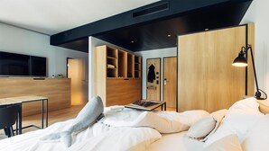 A modern hotel room with a bed, a desk, a wardrobe, and a TV.