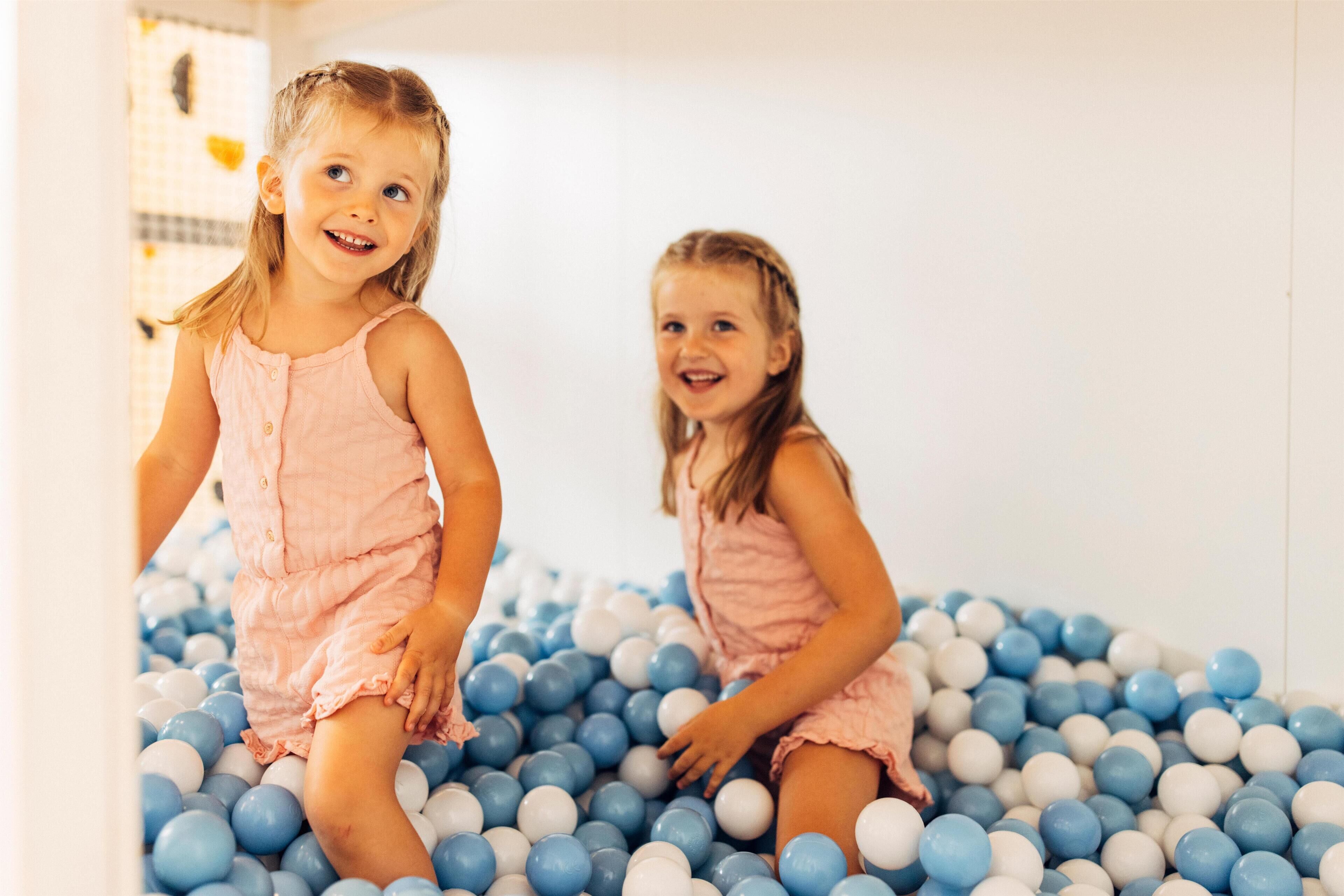 Two children playing in a ball pit filled with blue and white balls.