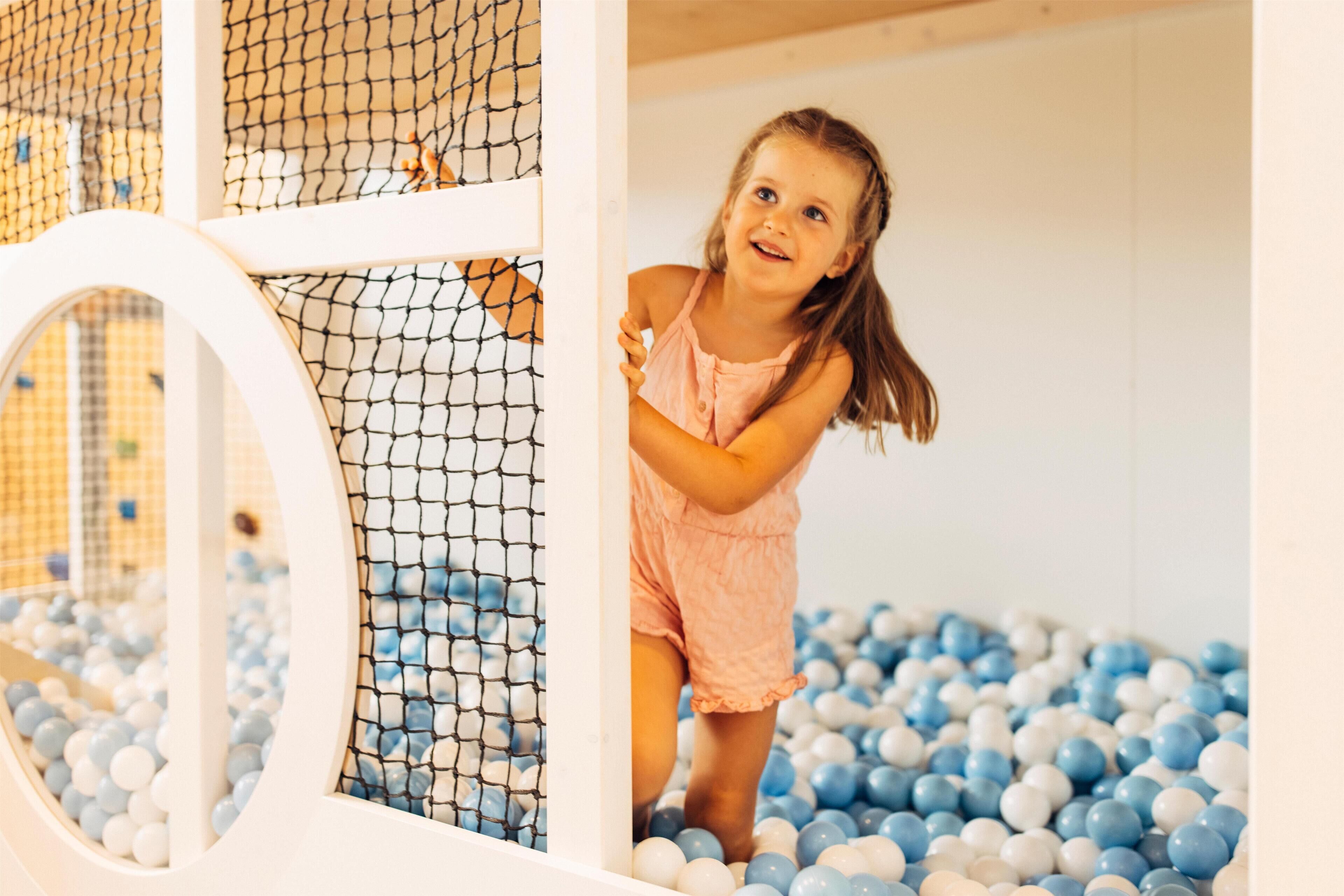 Een kind speelt in een ballenbak met witte en blauwe ballen, omgeven door een omheind speelgebied.