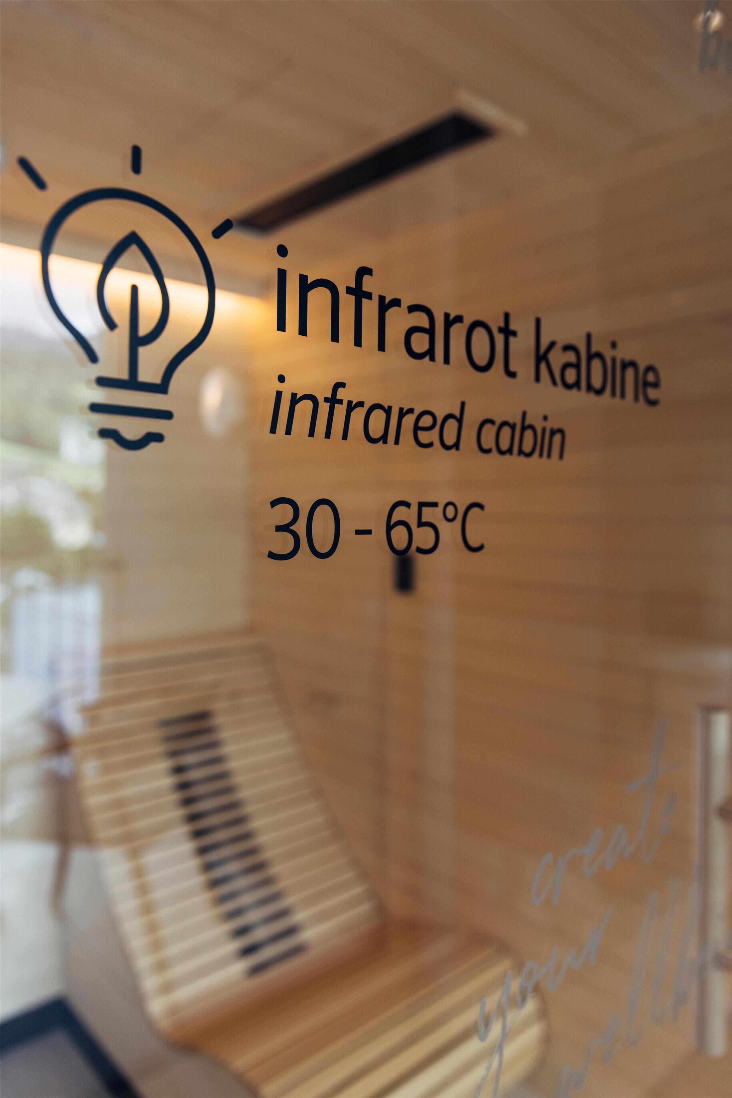 Une cabine à infrarouges dont la température varie de 30 à 65 °C, dotée d’un intérieur en bois et d’un lit avec une tête de lit.