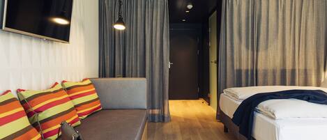 A modern hotel room with a sofa, a bed, a TV, and a view of the hallway.
