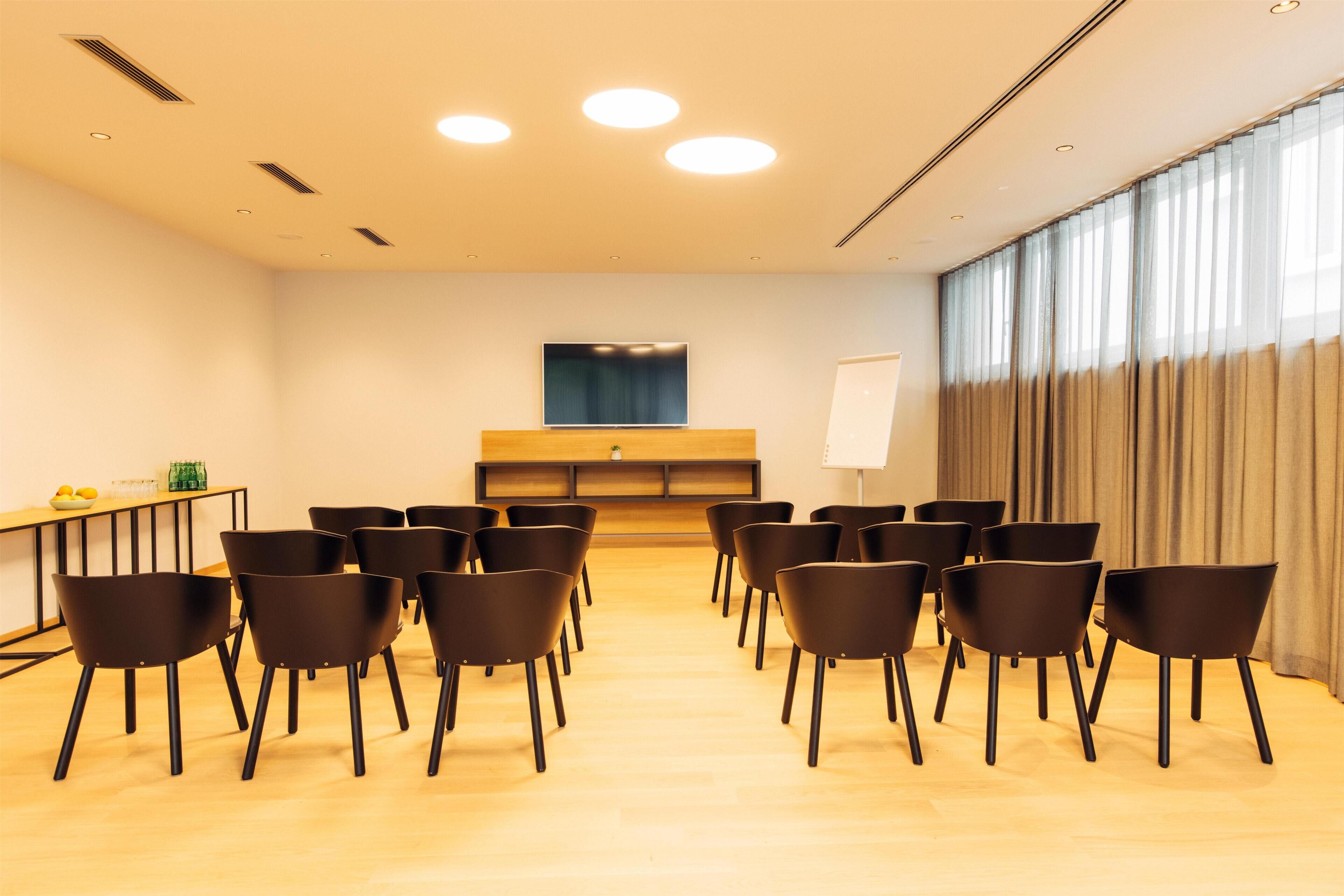 Un salón de conferencias con una larga mesa, varias sillas, una pizarra y un ventanal con cortinas.