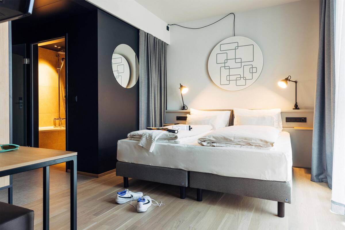 Ein modernes Hotelzimmer mit Bett, Nachttischen, einem Schreibtisch und einer Duschkabine.