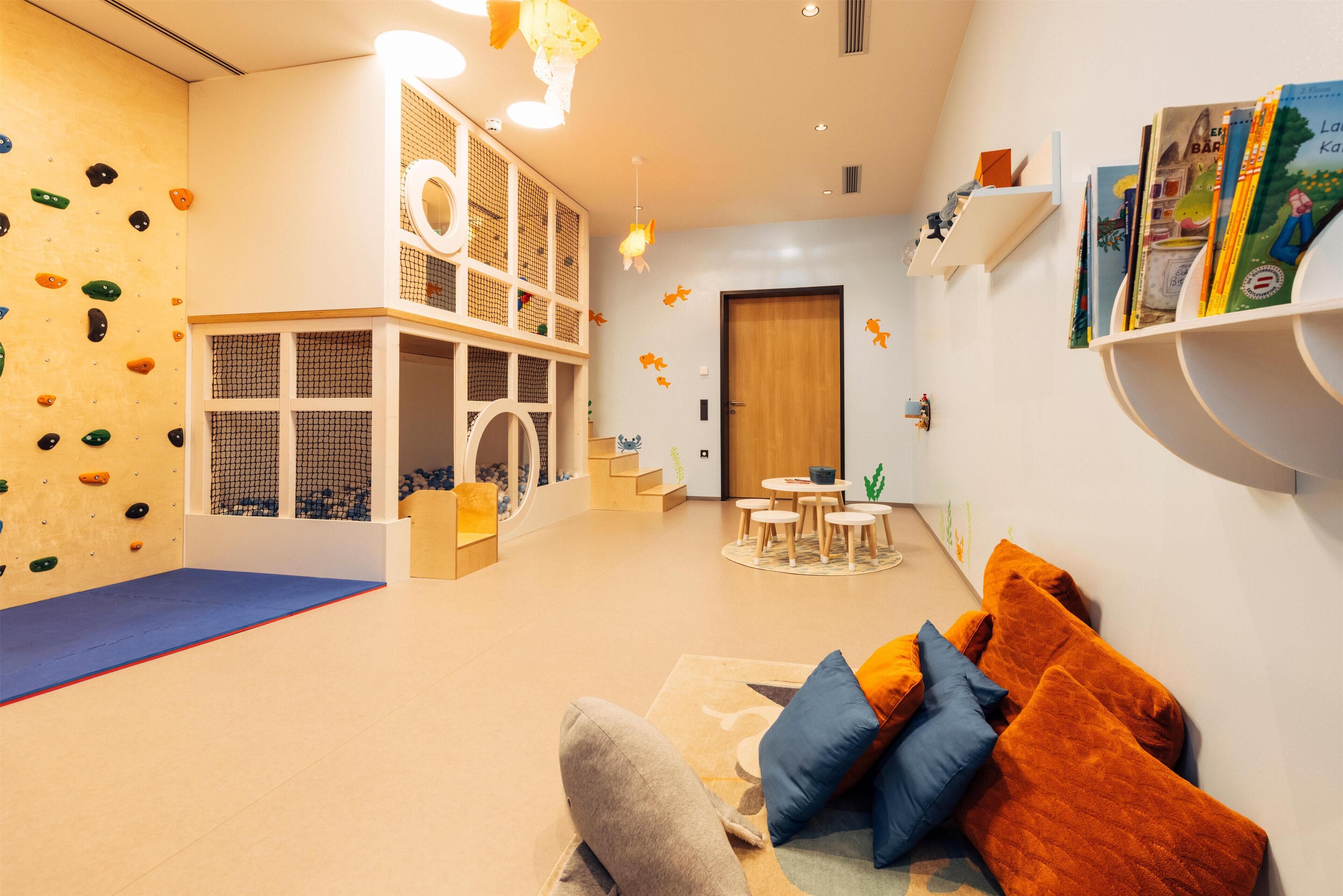 Une salle de jeux équipée d’un mur d’escalade, d’une cabane et d’un coin lecture avec des étagères à livres.