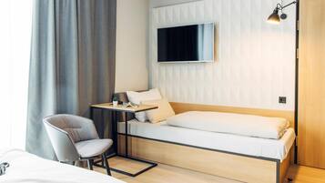 Una habitación de hotel moderna con una cama, un escritorio con una silla, un televisor montado en la pared y una puerta de madera.