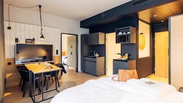 Una habitación de hotel moderna con una cama, un escritorio con sillas, una kitchenette y un televisor.