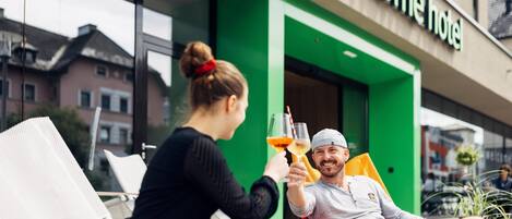 Due persone brindano con delle bevande davanti a un hotel con facciata verde.