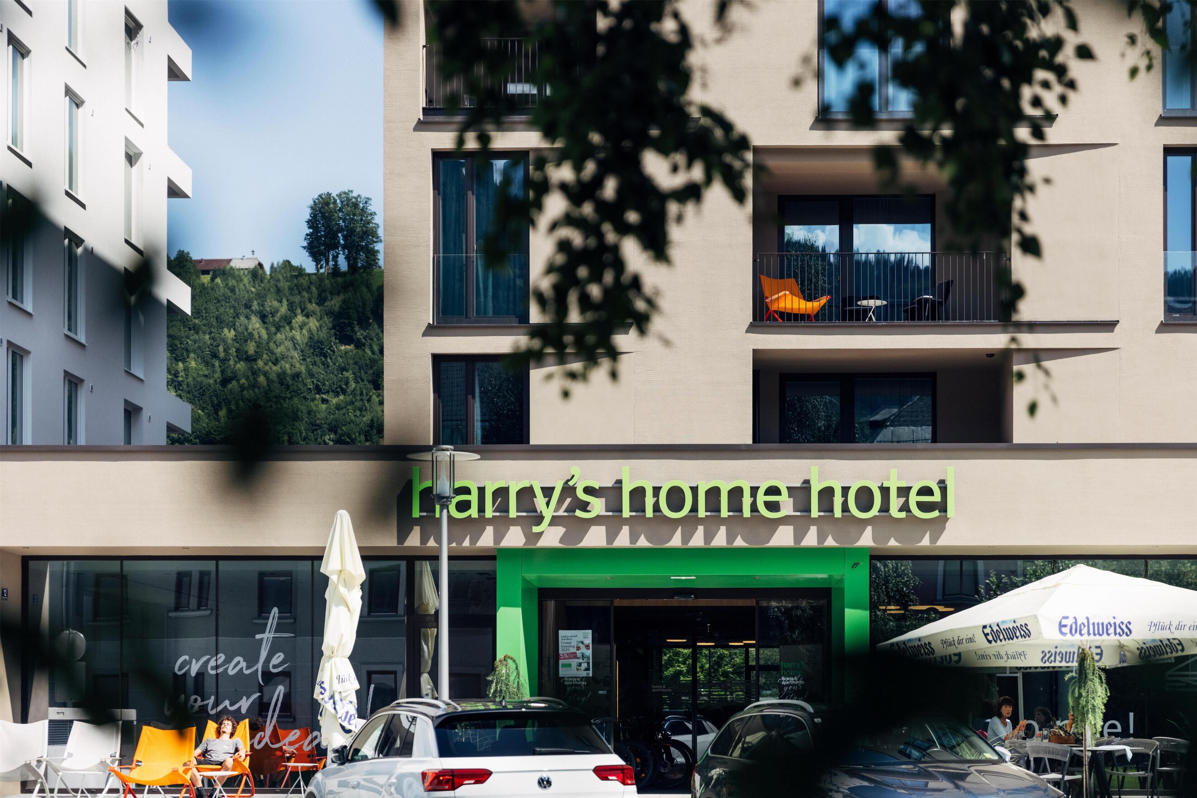 A hotel named "Harry's Home Hotel" with a green entrance, outdoor seating, and a view of a hill.