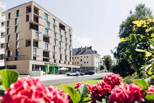 Un hotel de varios pisos con un diseño moderno, con balcones y un escaparate con plantas.