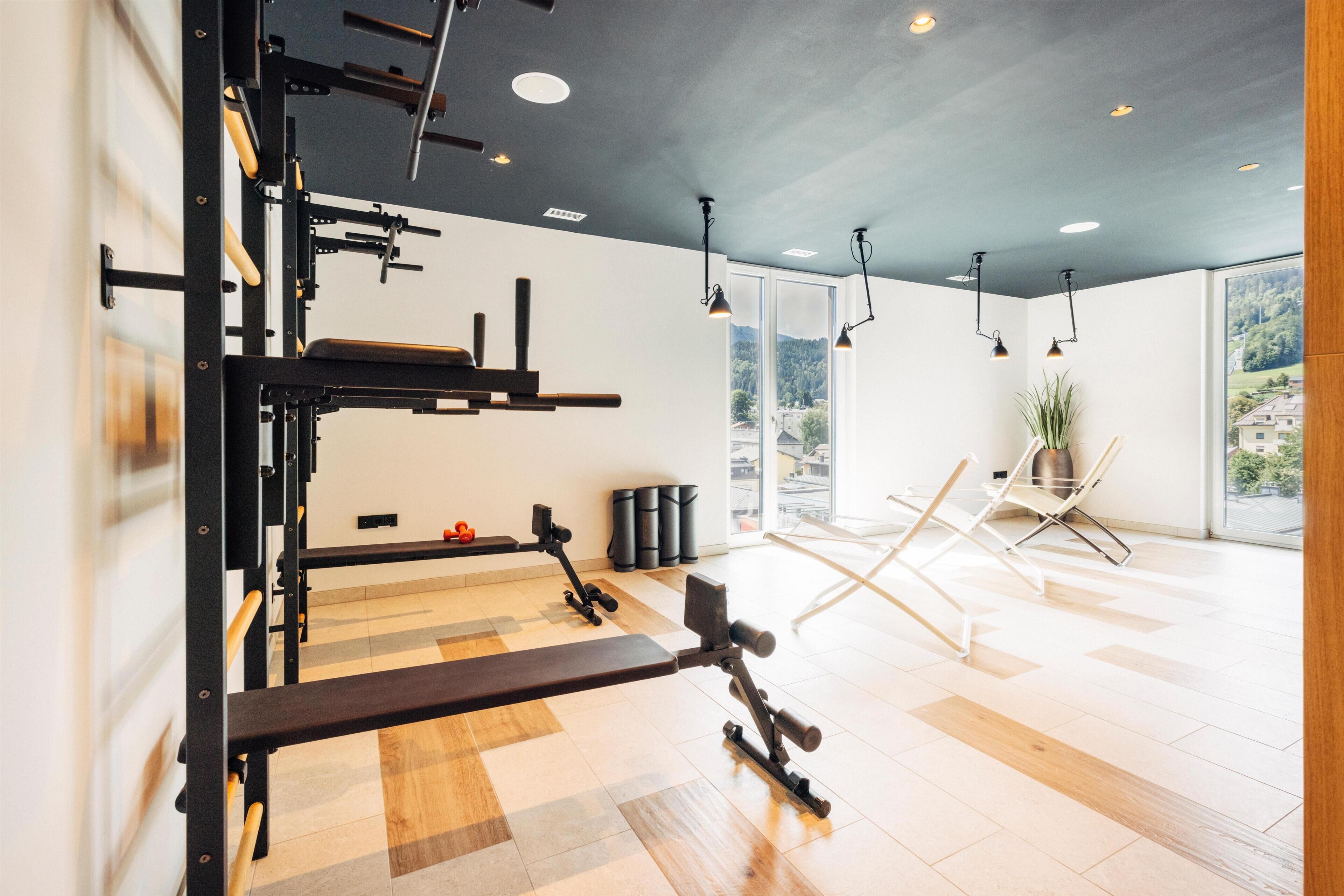 A gym with exercise equipment, a bench, and a large window with a view of trees and buildings.