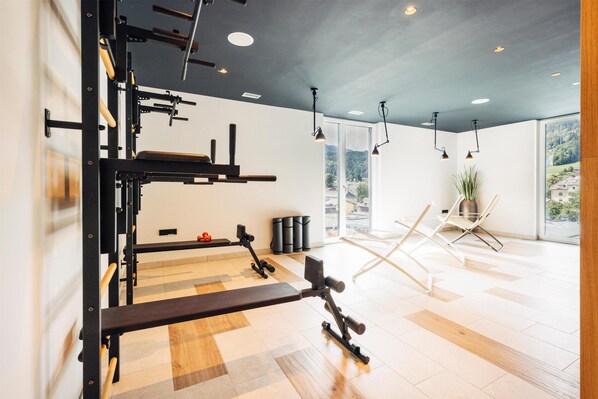 Un gimnasio con equipo de ejercicio, una banca y un ventanal con vistas a árboles y edificios.