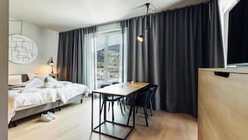 A modern bedroom with a bed, bedside table, lamp, and a view of the outdoors through large windows.