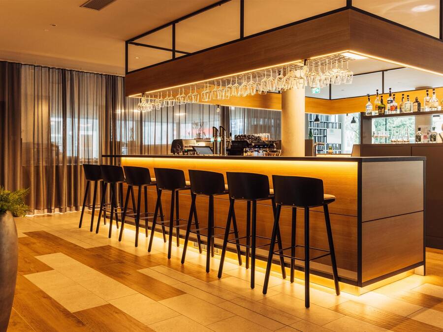 Un área de bar moderna con una barra larga, varios taburetes y una estación de barista.