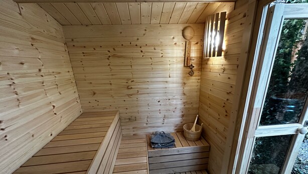 Un sauna en bois avec un banc, un seau et un luminaire fixé au mur.
